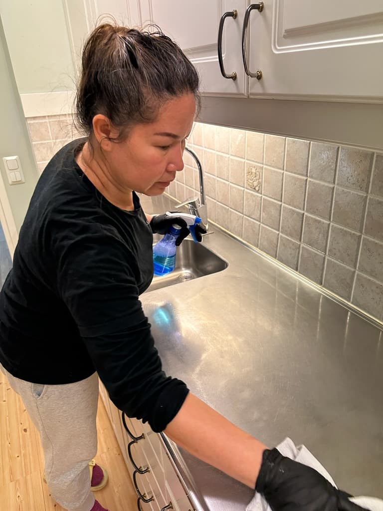 Medarbetare i PK Städservice-tröja städar rostfri köksbänk — trygg och igenkännbar service.