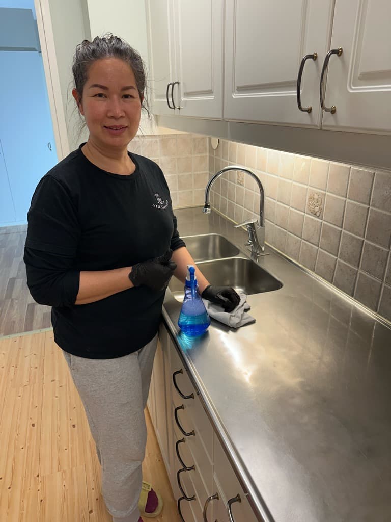 Hemstädning: medarbetare använder spray och trasa på rostfri diskbänk i kök.